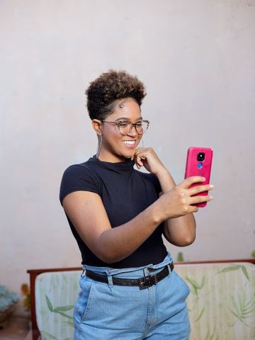 Mulher tirando selfie com o celular longe do rosto, de corpo quase inteiro